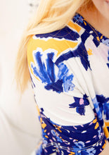 Load image into Gallery viewer, Closeup on the shoulder area of the Alexa Pajama Set in Whimsical Floral. The shirt sleeve and neckline contrast the main pajama fabric in Alivia Wildflower Burst Blue which features dark blue with yellow, white, pink, and light blue flowers and petals and white double stitched hemlines. 