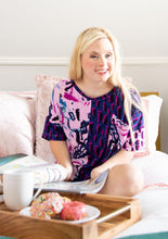 Load image into Gallery viewer, An interior shot of a model sitting cross-legged on a bed with an open magazine and breakfast tray with donuts. The neckline of the Alex Pajama Set top is scooped and the fabric and pocket square are a relaxed, slouchy fit. 