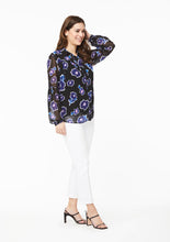 Load image into Gallery viewer, Partial front side view. The Vicki Shirt in Alivia Poppy Play Black sheer fabric has a relaxed fit without looking too bulky. With the top button undone, the shirt has a high v-neckline just below the collar bone. The hem of the Vicki Shirt falls at the hip a few inches below the hem of the solid black camisole top, showing the trousers through the sheer fabric.