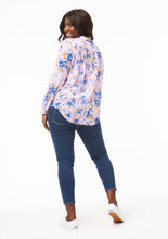 Load image into Gallery viewer, A model shows the back view of the Vicki Shirt in Wildflower Burst Orchid. They are leaning on one foot, pushing one hip to the side,and looking over their shoulder at the camera. The pleats and scooped tail of the shirt add shape and dimension to the airy fabric, creating a loose, flowy look.