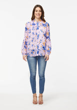 Load image into Gallery viewer, Front view. Alivia’s Vicki Shirt in Wildflower Burst Orchid. A model with light skin shows the shirt paired with light blue skinny jeans and brown strappy heels. The fabric is pale pink with scattered light and dark blue and canary yellow wildflowers. The blue flowers compliment the blue jeans.