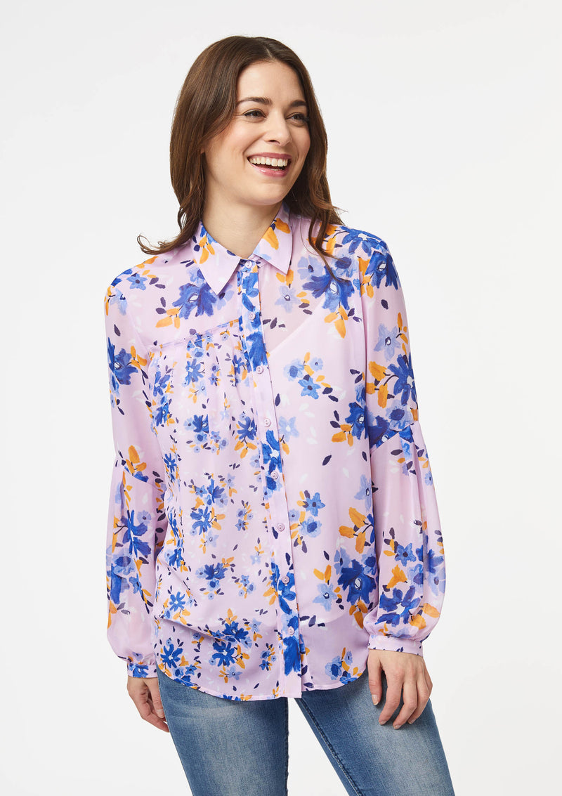 A person models the closeup front view of the Vicki Shirt in Wildflower Burst Orchid. The model’s arms are resting at their sides and the shirt is buttoned all the way to the top, creating a clean v-line at the base of the neck.