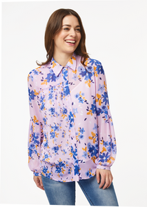 A person models the closeup front view of the Vicki Shirt in Wildflower Burst Orchid. The model’s arms are resting at their sides and the shirt is buttoned all the way to the top, creating a clean v-line at the base of the neck.
