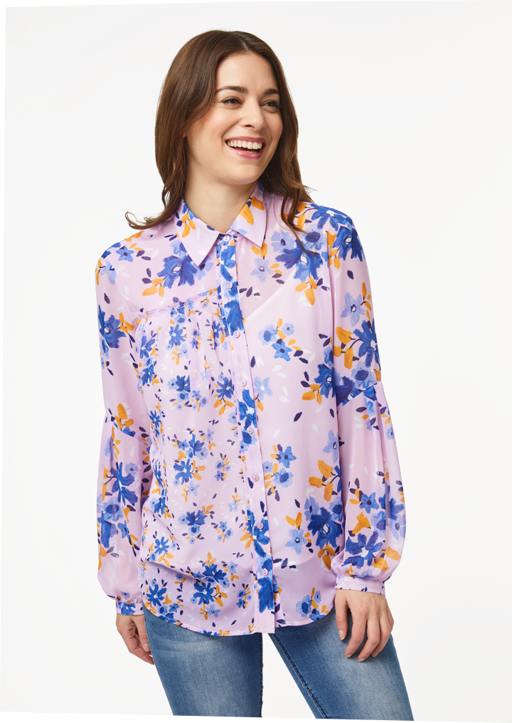 A person models the closeup front view of the Vicki Shirt in Wildflower Burst Orchid. The model’s arms are resting at their sides and the shirt is buttoned all the way to the top, creating a clean v-line at the base of the neck.